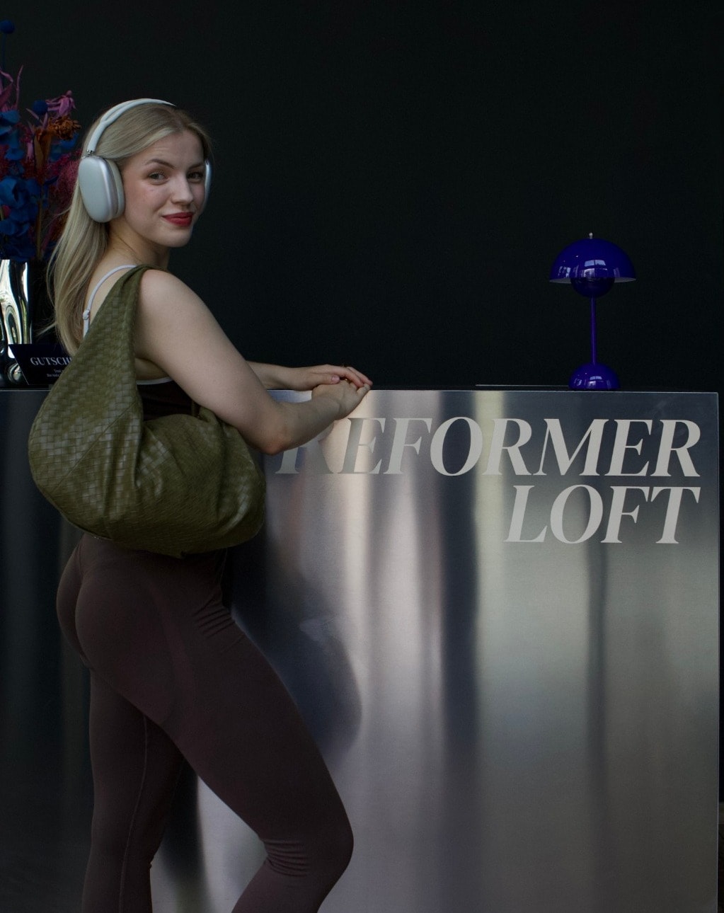 Eine Besucherin mit Kopfhörern und Tasche lächelt am Empfang des Reformer Loft